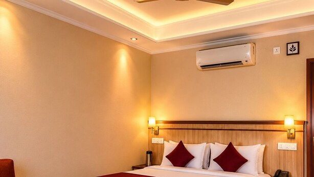 Une chambre d’hôtel comprenant un lit, des tables de chevet, une chaise, une petite table avec une plante et un appareil de climatisation.