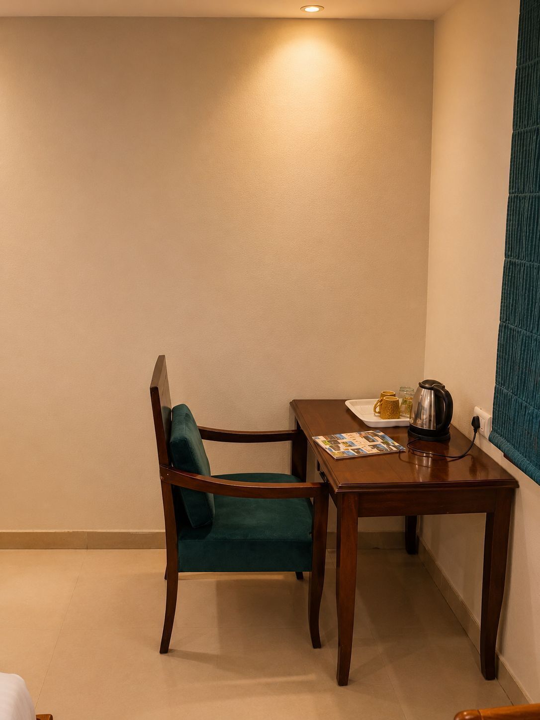 Una habitación pequeña con una mesa de madera, una silla, una tetera y una ventana con cortina verde.