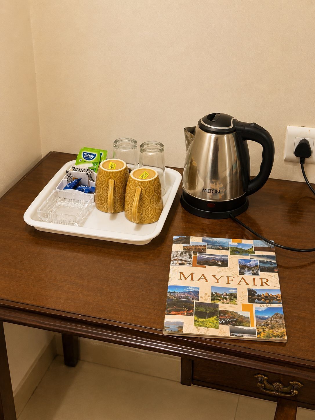A tray with a kettle, two patterned mugs, and tea packets on a wooden table.