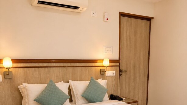 Una camera d'albergo con un letto, comodini, un condizionatore d'aria, lampade a parete e una porta in legno.