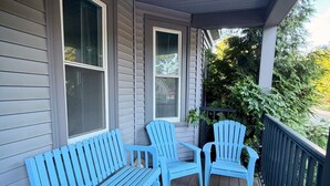 A porch with a wooden floor, a blue Adirondack chair, a blue bench, and a potted plant.