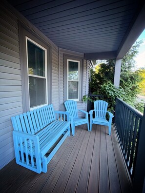 A porch with a wooden floor, a blue Adirondack chair, a blue bench, and a potted plant.