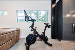 Un espacio interior con una bicicleta estática, un sofá de cuero marrón y una ventana que da a zonas verdes.