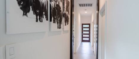 A hallway with a series of black and white photographs on the wall, a door at the end, and a light switch on the wall.