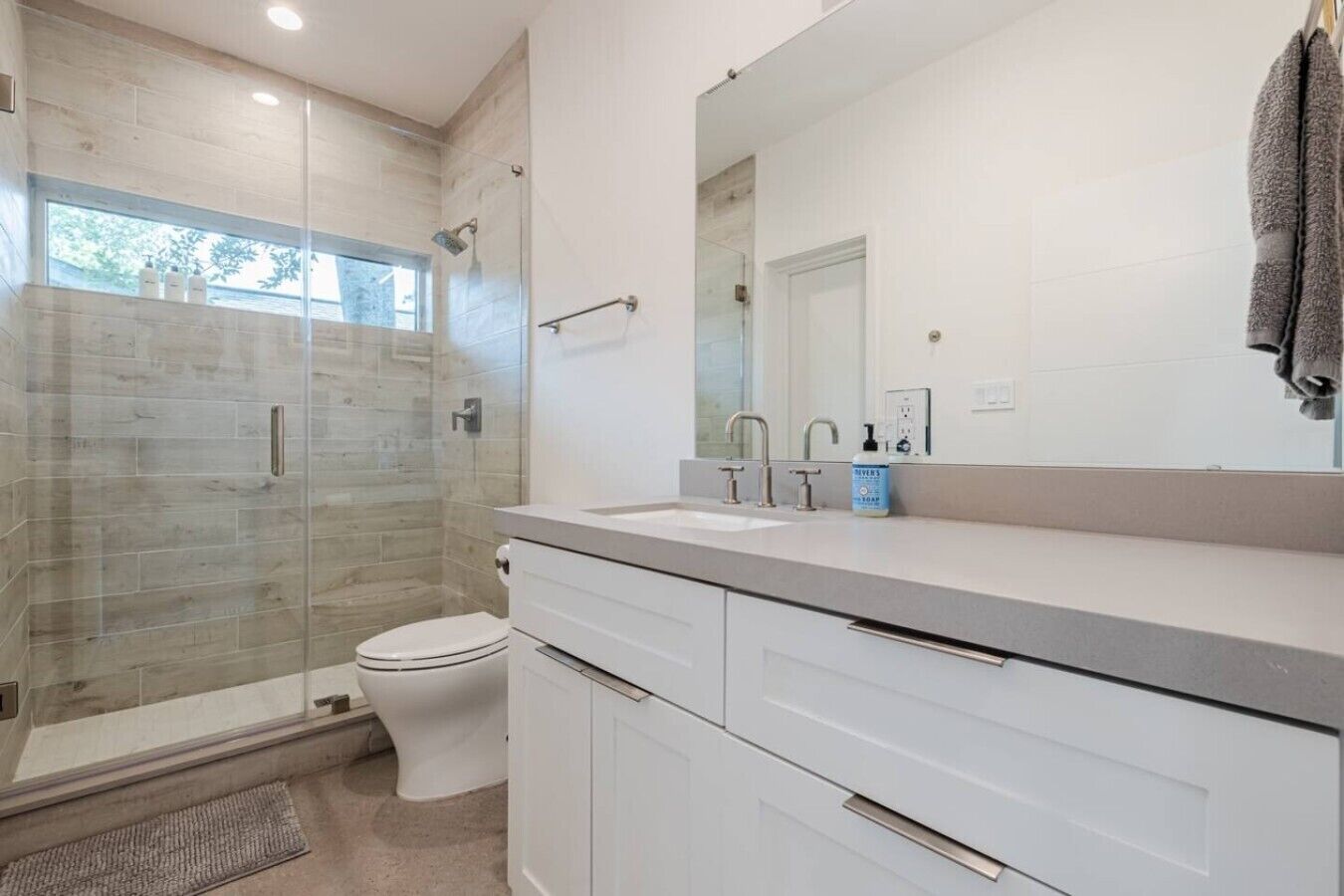 A modern bathroom with a glass shower enclosure, a toilet, a sink with a large mirror, and a towel hanging on the wall.