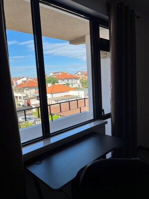 Ein Zimmer mit großem Fenster, Schreibtisch und Blick auf Gebäude mit roten Dächern.