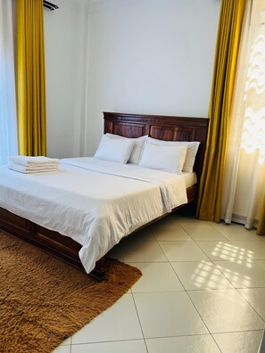 A neatly made bed with white linens and pillows, a wooden headboard, and a brown furry rug on a tiled floor. - Cozy 1-bedroom apartment in serene Kampala, price is negotiable (Kampala)
