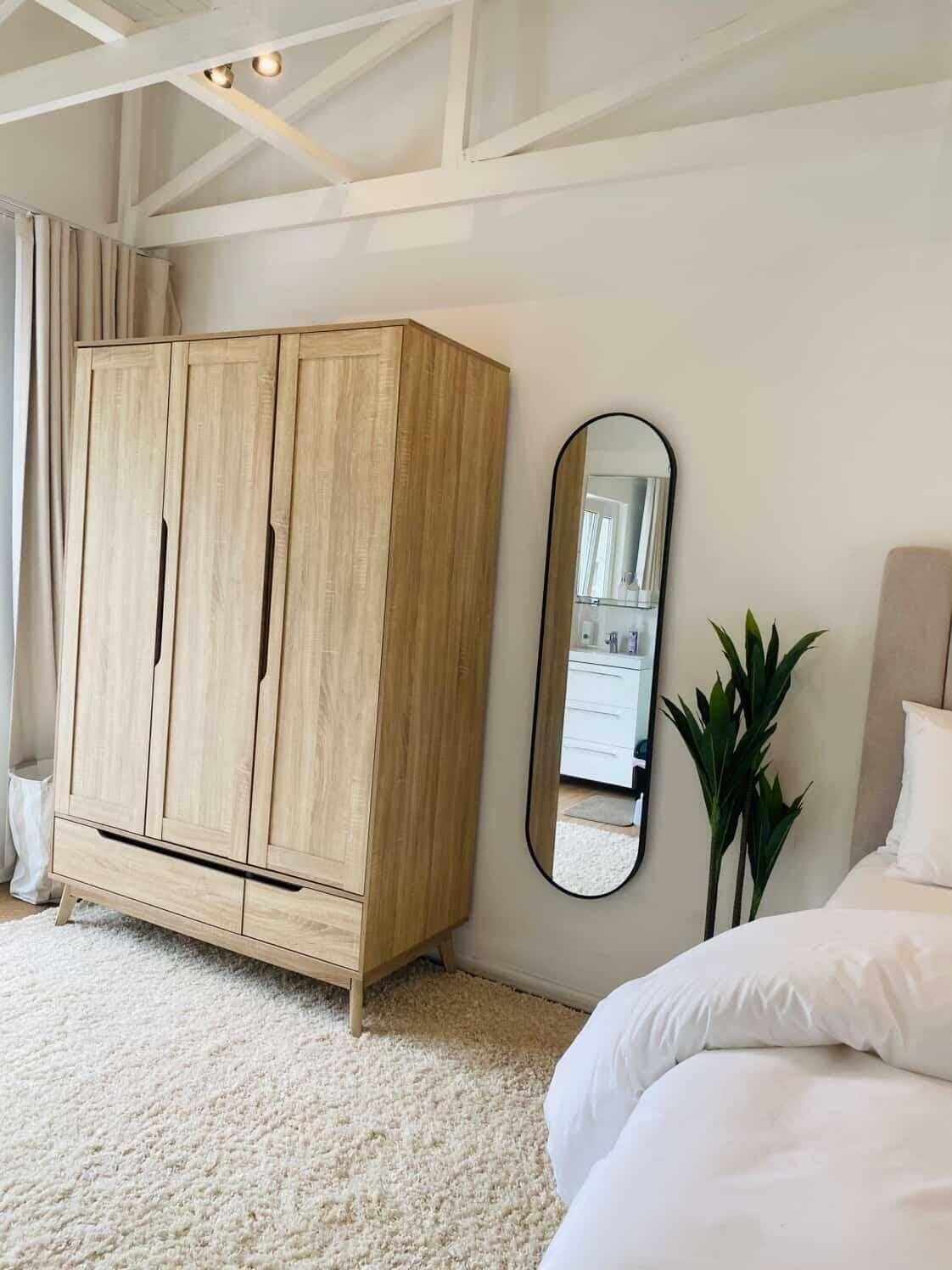 Ein Schlafzimmer mit großem Kleiderschrank, einem Bett, einem Spiegel und einer Topfpflanze.
