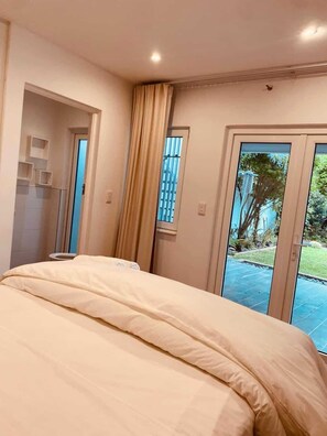 Ein Schlafzimmer mit einem großen Bett, einer Tür, die auf einen Balkon führt, und Blick ins Freie.