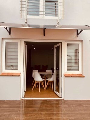 Fachada moderna con un área de comedor visible a través de una puerta abierta, que incluye una mesa y sillas.