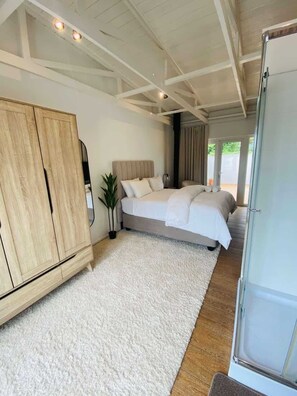 Un dormitorio con un armario amplio, una cama con muchas almohadas, una planta en maceta y vistas a través de un ventanal.