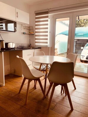 Una cocina moderna con comedor, que incluye una mesa redonda y sillas, una ventana con persianas y vistas a un coche estacionado fuera.
