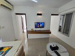 A modern living room with a flat-screen TV, a wooden console table, a dining table, and a large window. - Replay Comfortable Apartment (Bophut)