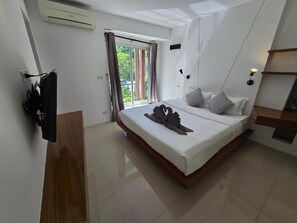 Moderni hotellihuone, jossa on suuri sänky, televisio ja liukuovet, jotka johtavat ulos.