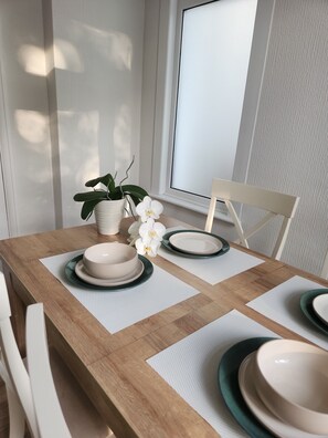 Een eettafel met witte borden, een kamerplant en een raam met zonwering.