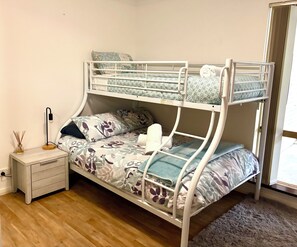 Ein Stockbett mit Blumenmuster, ein Nachttisch mit Lampe und ein Fenster mit Vorhängen.