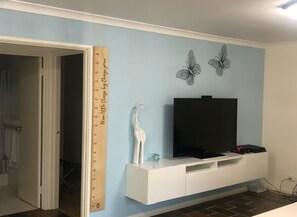A room with a TV on a white entertainment unit, a giraffe figurine, and a ruler on the wall. - Raylea Retreat - Rest and Relax surrounded by nature - fur baby friendly!! (Denmark)