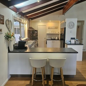 A modern kitchen with a central island, two bar stools, a clock, and a heart-shaped decoration on the wall.