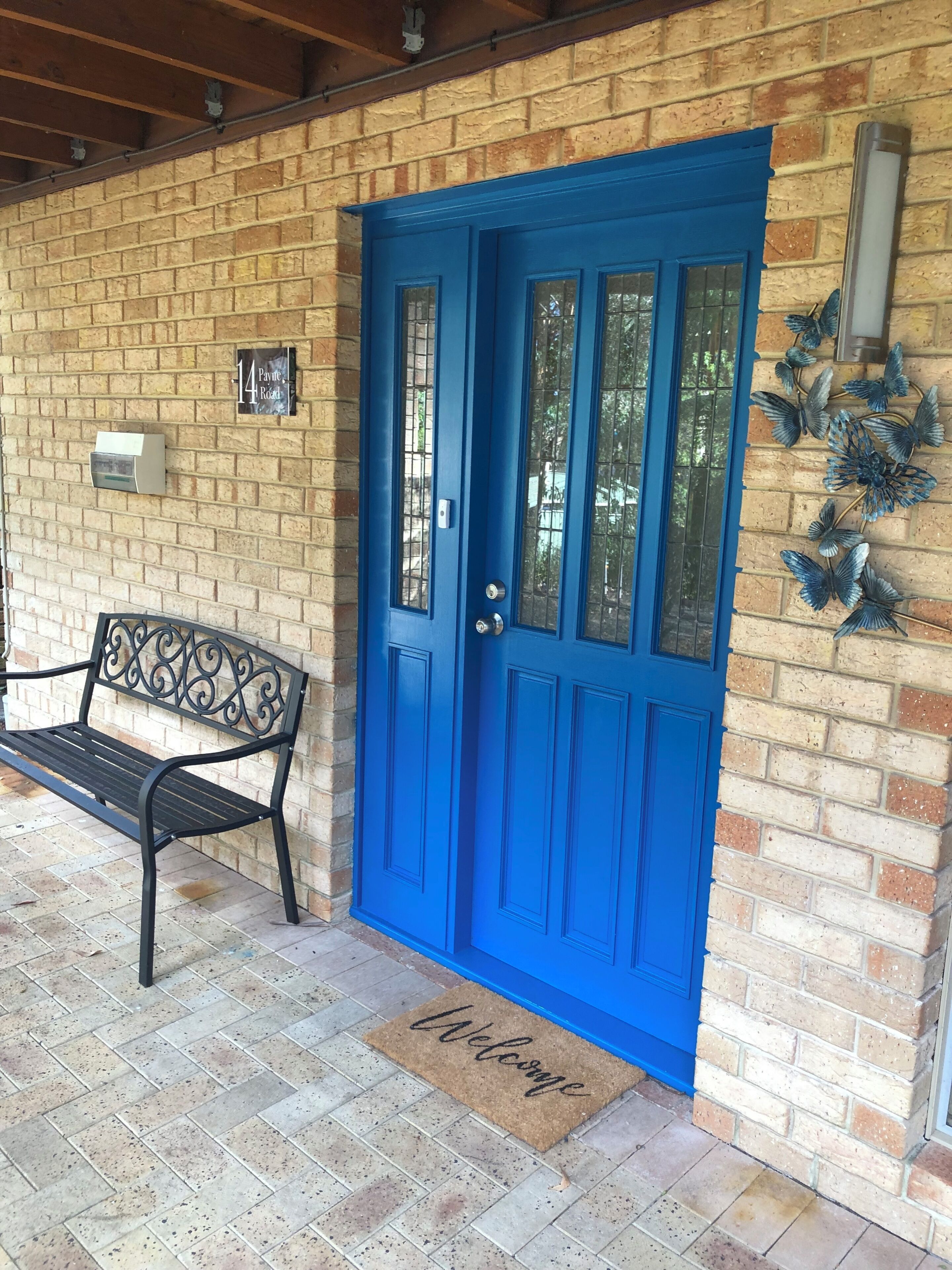 A blue door with a doormat, a bench, and a wall-mounted light fixture.