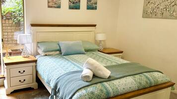 A bedroom with a wooden headboard, a bed with patterned bedding, a nightstand with a lamp, and artwork on the walls.