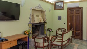 A living room with a fireplace, two wooden chairs, a wooden desk, a television, and a door. - B&B Gioiosa (Gioiosa Ionica)