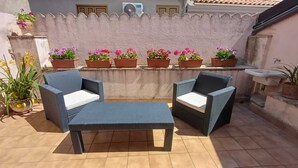 A patio with two wicker chairs and a small table, surrounded by potted plants and a tiled floor. - B&B Gioiosa (Gioiosa Ionica)