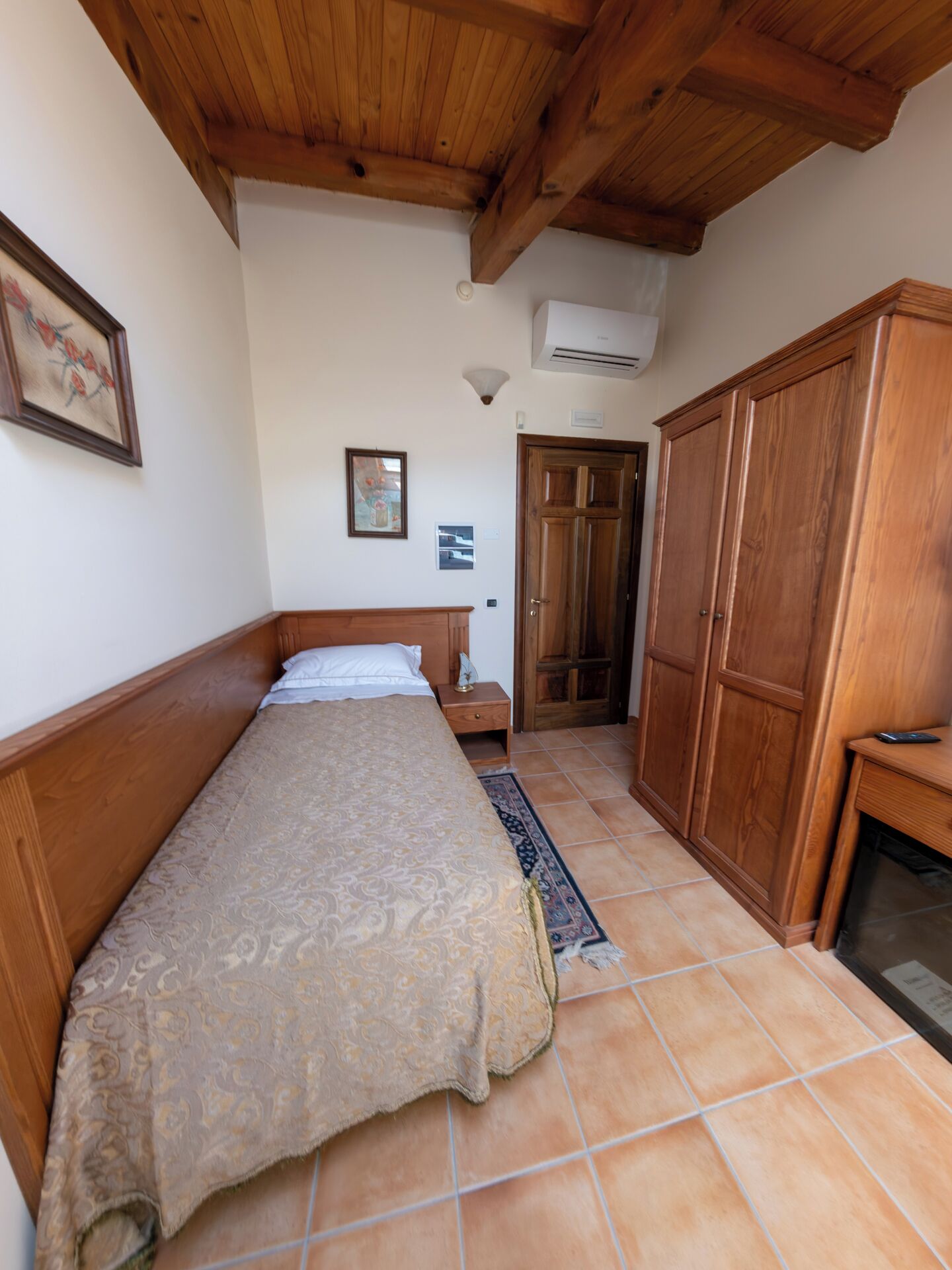 A bedroom with a bed, wooden wardrobe, and a tiled floor.