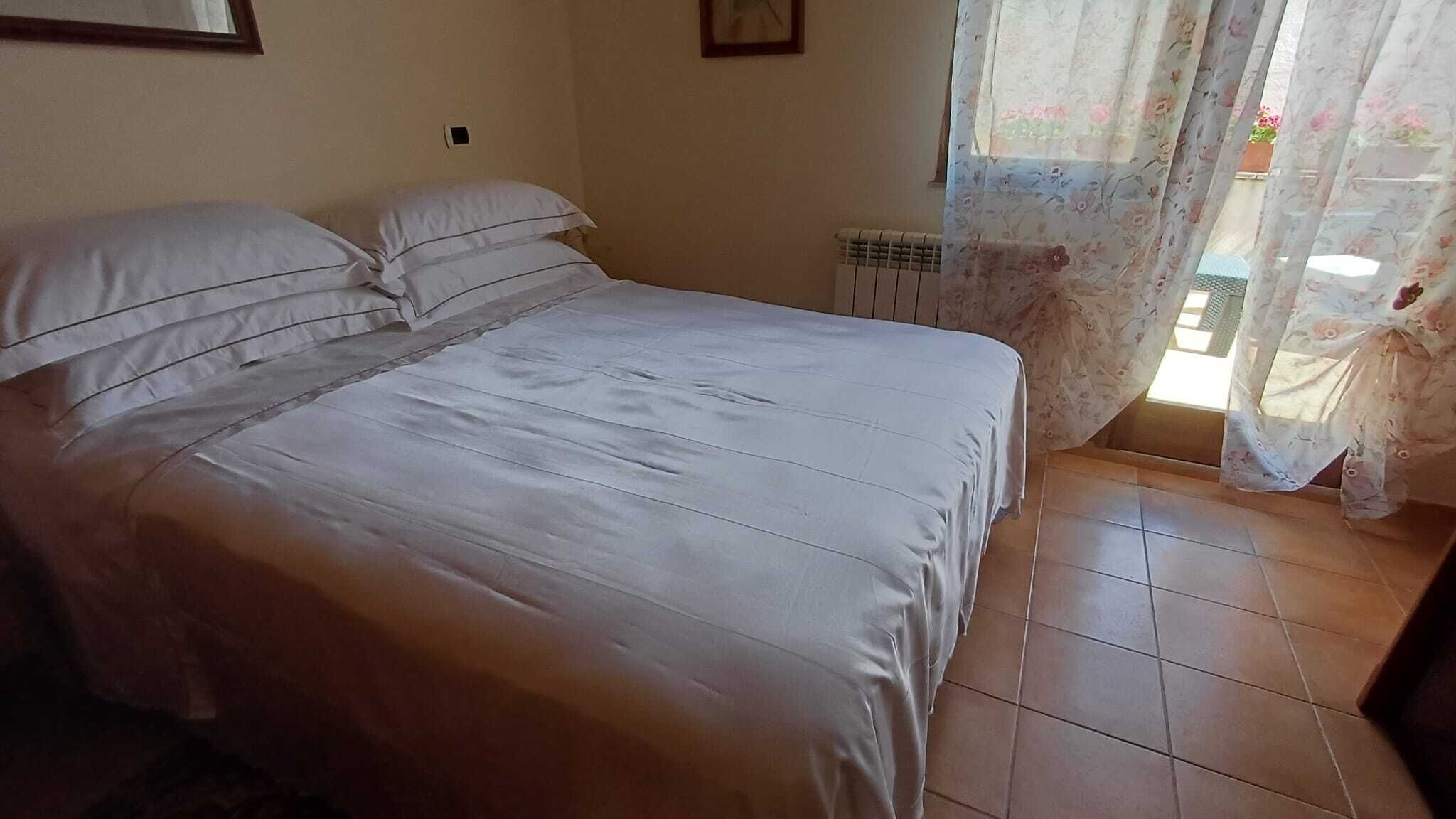 Ein Schlafzimmer mit einem Bett, einem Heizkörper und einem Fenster mit blumigen Vorhängen.
