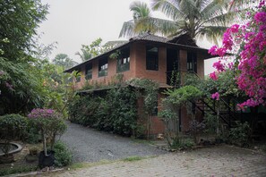 A traditional house with a brick exterior, surrounded by lush greenery and flowering plants. - Valhalla villa (panvel)