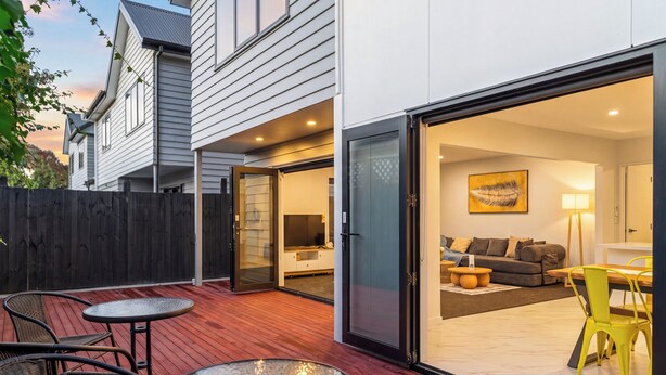Ein modernes Haus mit Terrasse und bodentiefen Fenstern, die in einen Wohnbereich mit Sofa, Tisch und Stühlen führen.