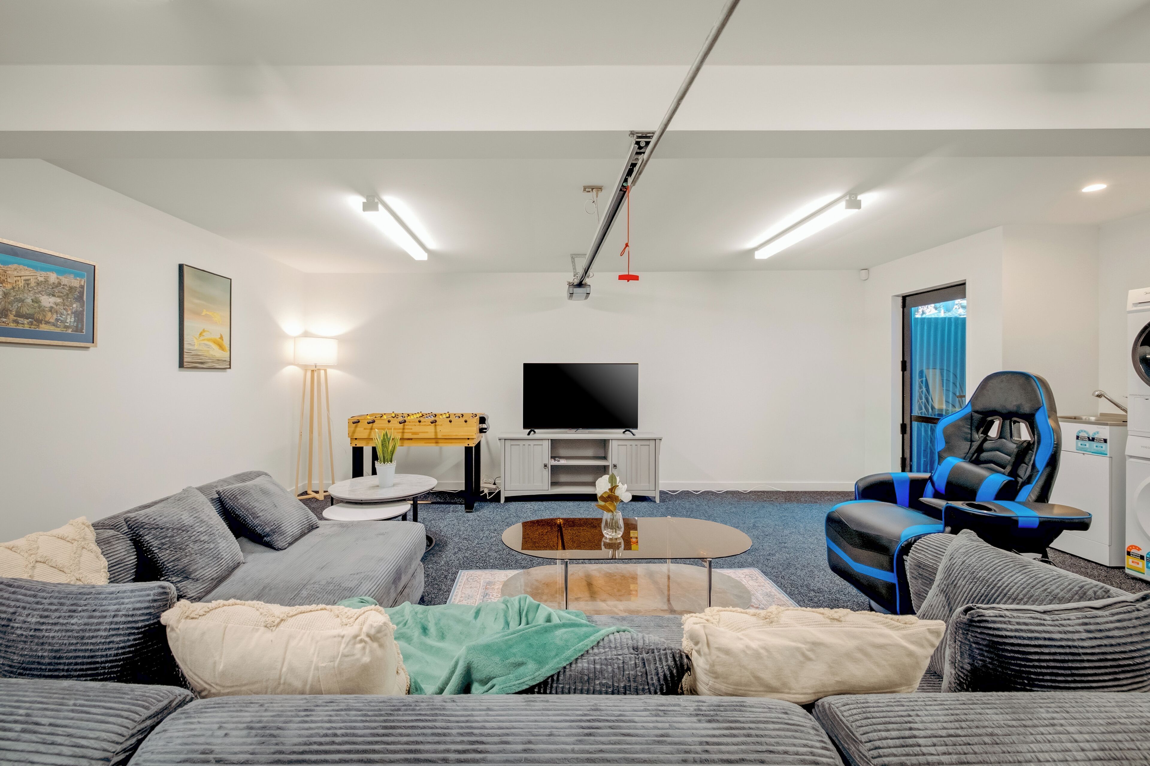 A modern living room with a sofa, coffee table, gaming chair, TV, and a ceiling-mounted device.
