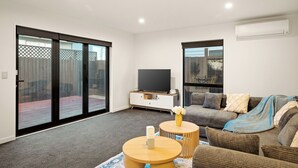 Ein modernes Wohnzimmer mit Flachbildfernseher, einer Couch, einem Couchtisch und einer Glastür, die zu einem Außenbereich führt.