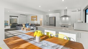 Eine moderne Küche mit weißen Schränken, einer Edelstahl-Dunstabzugshaube und einem Essbereich mit Holztisch und gelben Stühlen.