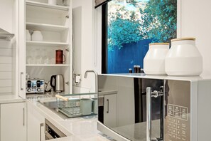 A modern kitchen with a built-in microwave, a coffee machine, and a window with a view of greenery.
