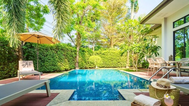A swimming pool with lounge chairs, a sun umbrella, and a wicker basket with towels and a drink. - Premium 3BR Pool Villa In Cherngthalay (Choeng Thale)