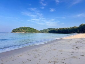 Ein Strand mit sandigem Ufer, ruhigem Wasser und einer bewaldeten Insel in der Ferne.