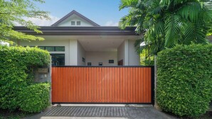 A modern house with a gated entrance, surrounded by lush greenery. - Premium 3BR Pool Villa In Cherngthalay (Choeng Thale)