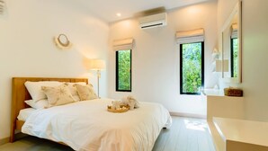 A bedroom with a wooden bed, a bedside table, a lamp, and a window with a view of greenery. - Premium 3BR Pool Villa In Cherngthalay (Choeng Thale)