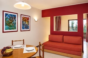 A dining area with a wooden table set for two, a red sofa, and two abstract paintings on the wall. - Huma by Umbral (Albufeira)