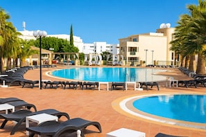 A swimming pool with lounge chairs and tables, surrounded by palm trees and buildings. - Huma by Umbral (Albufeira)
