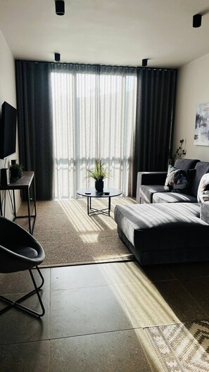 Ein modernes Wohnzimmer mit einer Couch, einem Couchtisch, einem Fernseher und einer Topfpflanze.