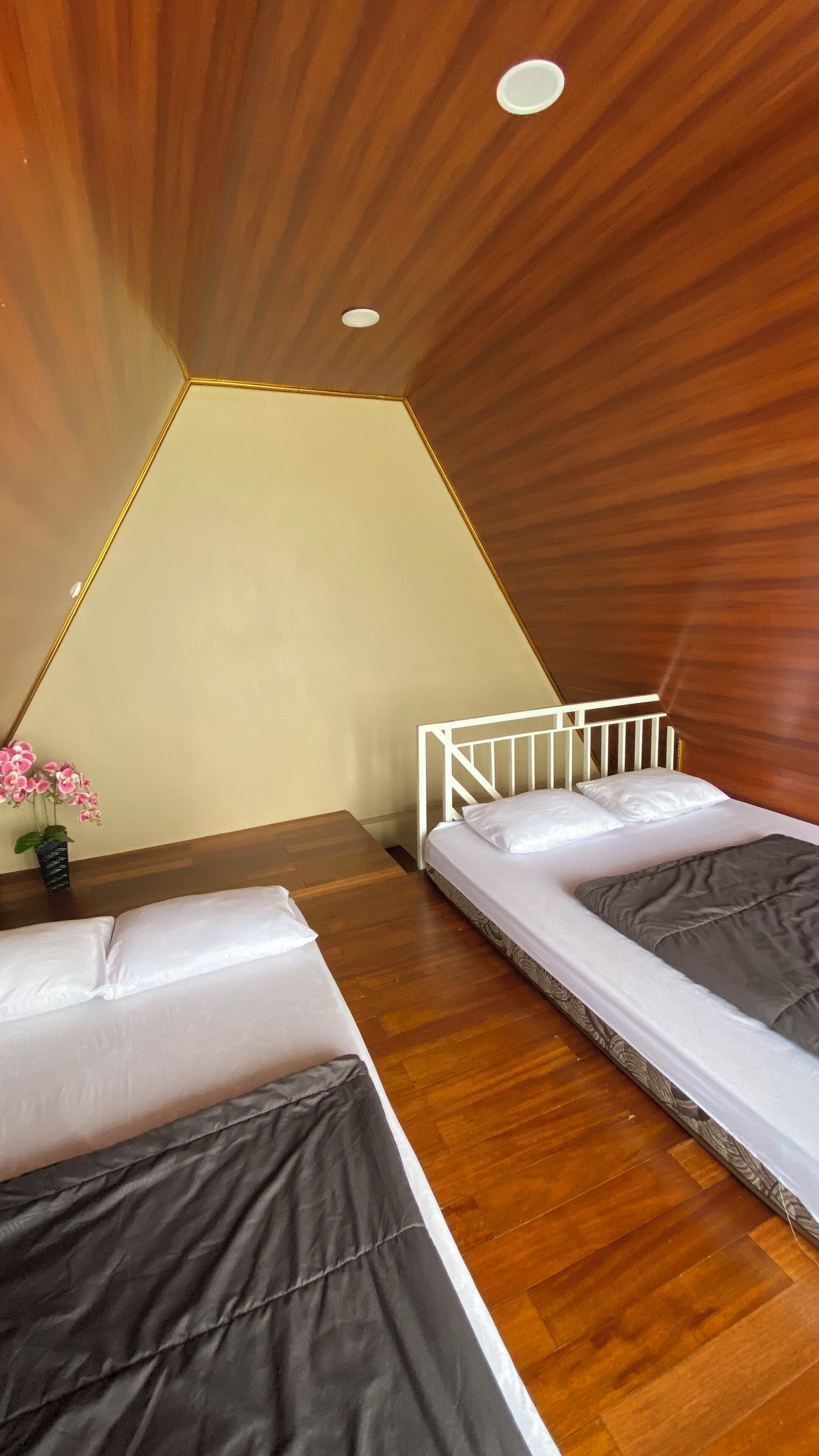 A room with two beds, a wooden ceiling, and a small table with a vase of flowers.