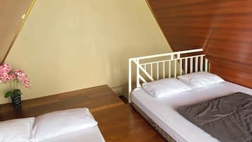 A room with two beds, a wooden ceiling, and a small table with a vase of flowers.