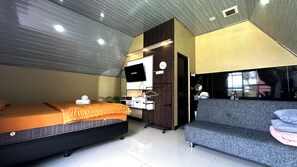 Habitación de hotel moderna con cama, sofá, televisor, una pequeña kitchenette y ventana.