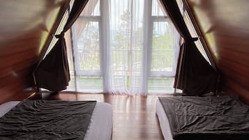 A room with two beds, a wooden ceiling, and a large window with curtains.