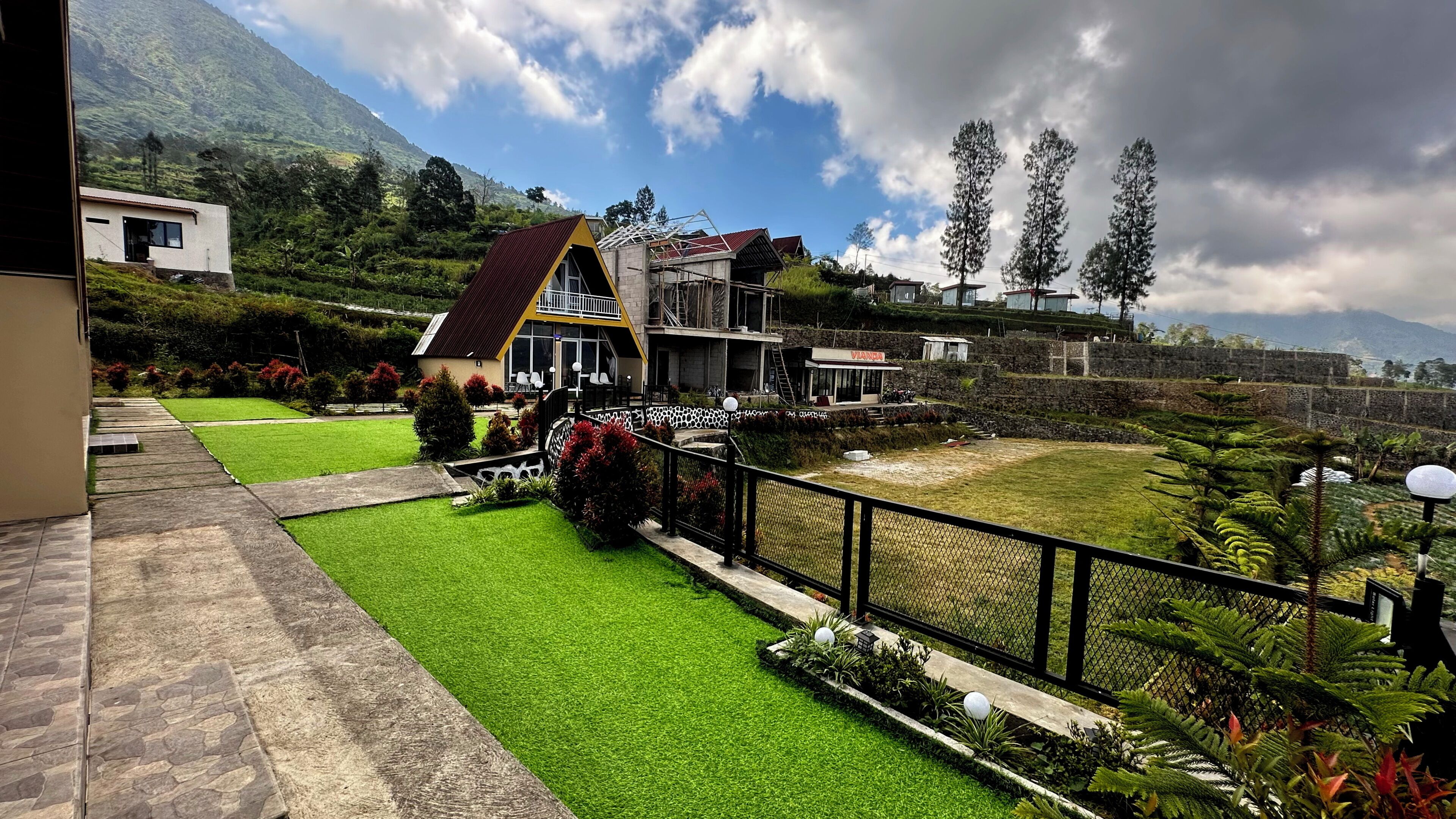 Ein Hotel mit gepflegter Rasenfläche, einem eingezäunten Garten und Blick auf eine Berglandschaft.