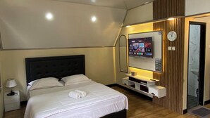 Habitación de hotel con cama, televisor, reloj y puerta del baño.