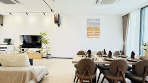A modern hotel room with a dining area, a flat-screen TV, a potted plant, and a painting of a sunset. - NORD House J21 (Banglamung)