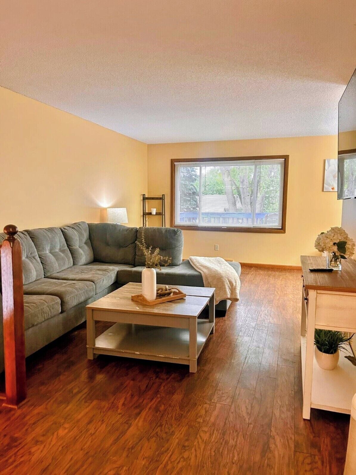 A living room with a sofa, coffee table, and a window with blinds.