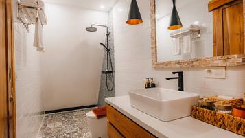 Un baño moderno con un lavabo blanco, tocador de madera y ducha con manguera negra.